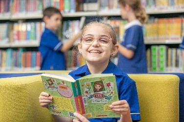 Student reading a book in a school library, supporting literacy development, enjoyment of reading and independent learning